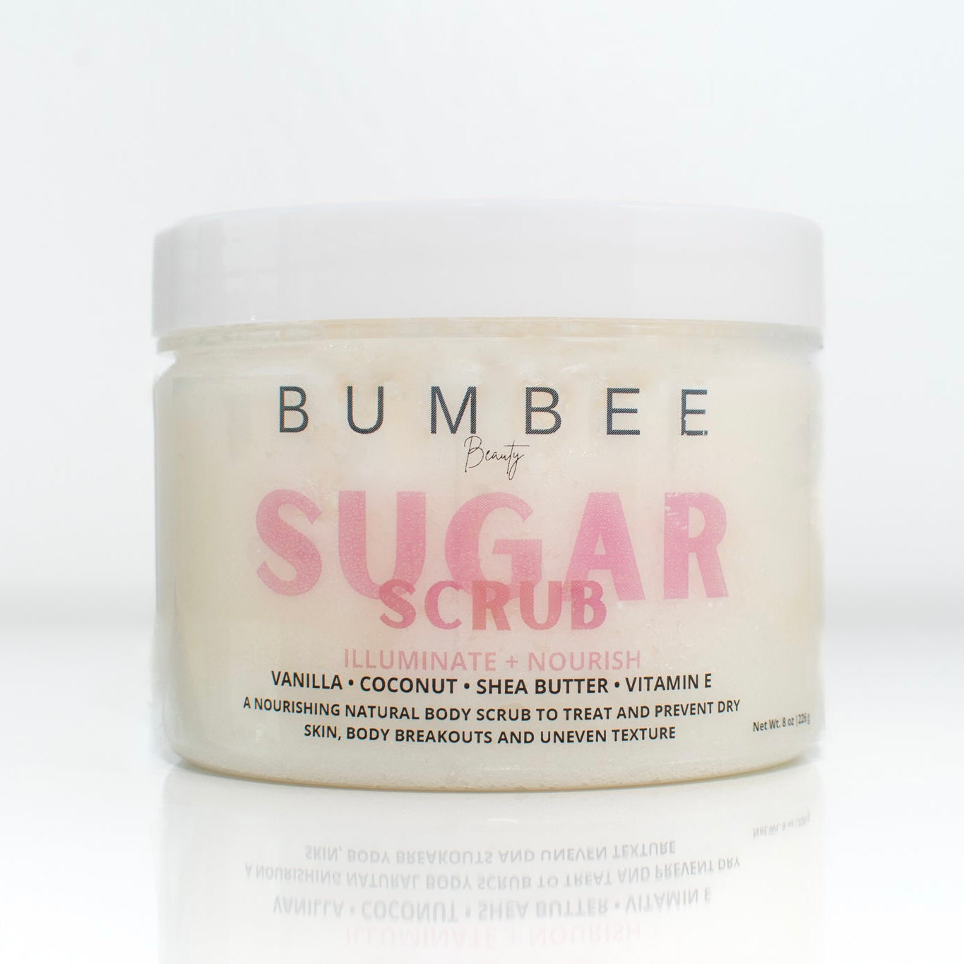 A jar of Bumbee Beauty Sugar Scrub with a white lid. The label reads 'illuminate and Nourish' and lists the ingredients as  coconut, shea butter, and vitamin E. The text below describes it as an nourishing natural body scrub to rest and prevent dry skin, body breakouts and uneven texture. The product has a white colour with pink and black text