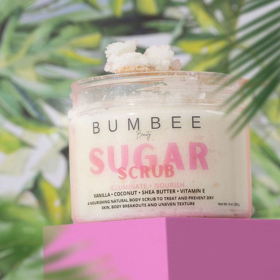 A jar of Bumbee Beauty Sugar Scrub placed in a tropical setting, with the scrub's textured surface visible on top of the Sugar scrub 8 oz Jar. The image evokes a sense of relaxation and indulgence, highlighting the product's natural ingredients and luxurious feel